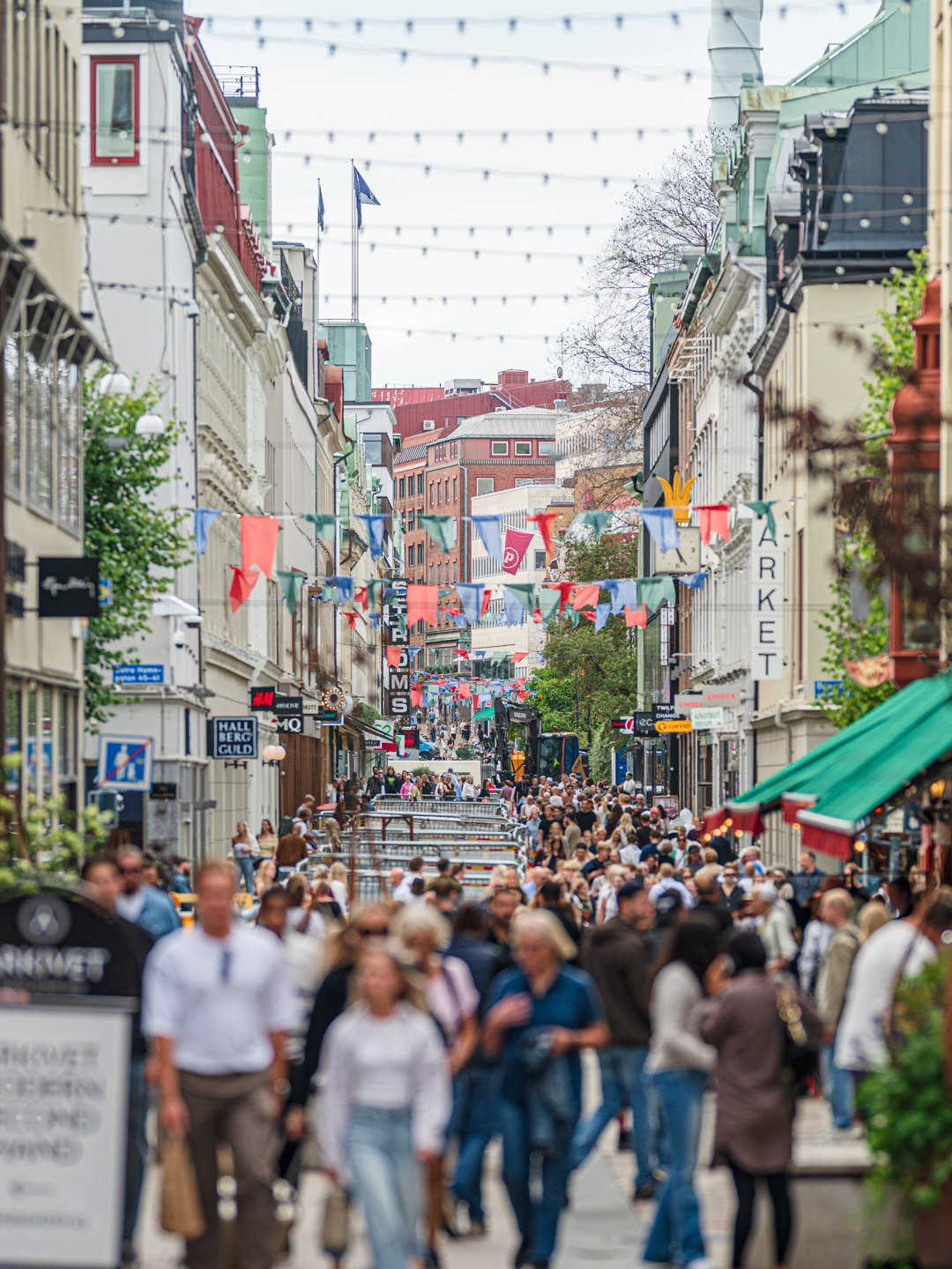 En folkmassa som går längs en gata bredvid höga byggnader.
