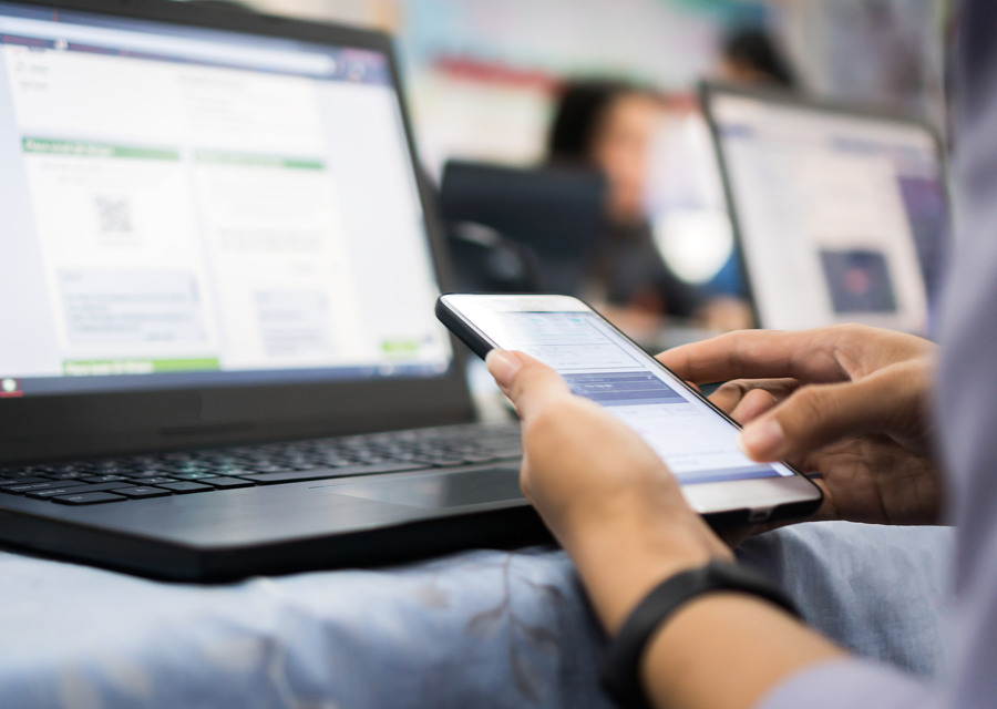 En person som sitter framför en bärbar dator och håller i en mobiltelefon.