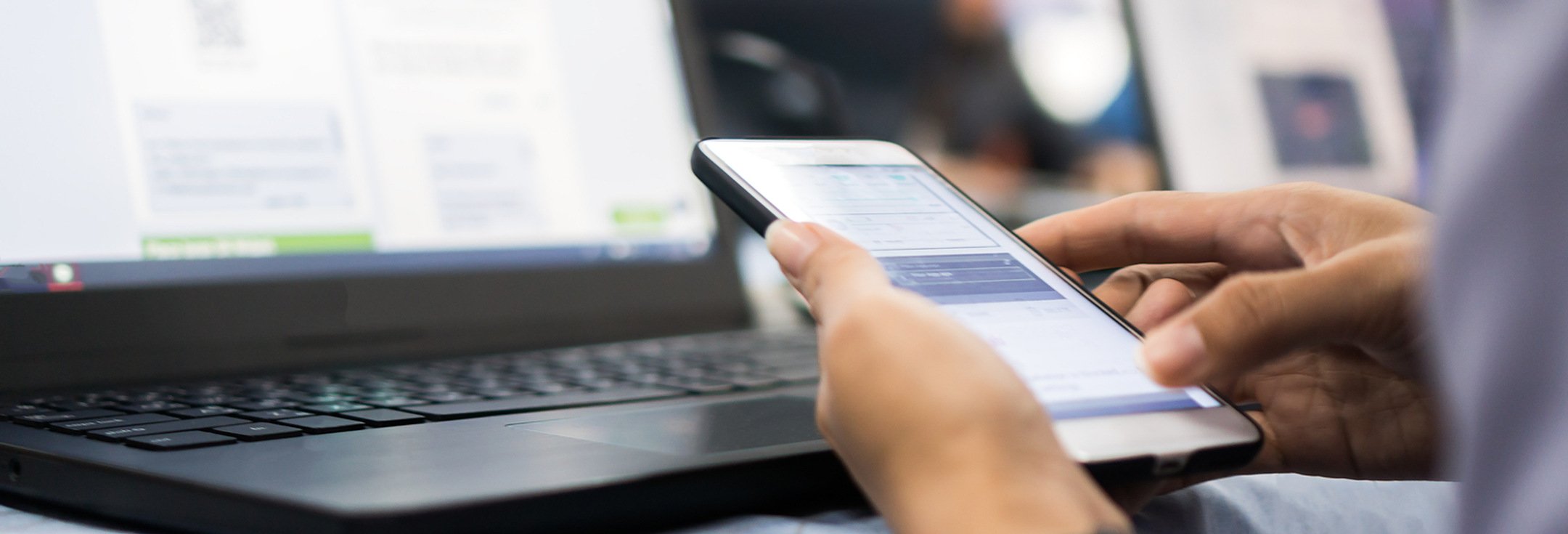 En person som sitter framför en bärbar dator och håller i en mobiltelefon.