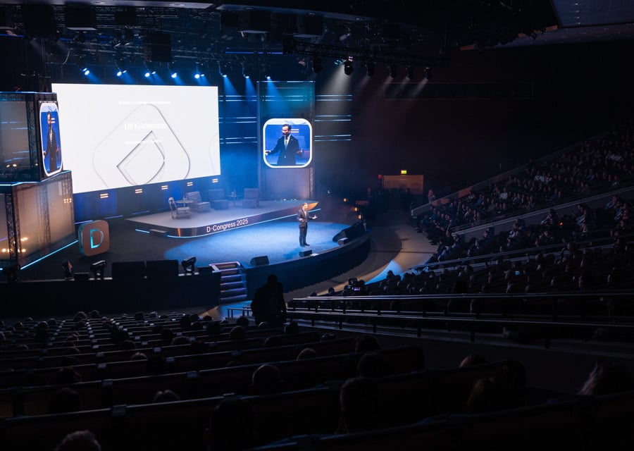 En man står på en scen framför en stor skärm.