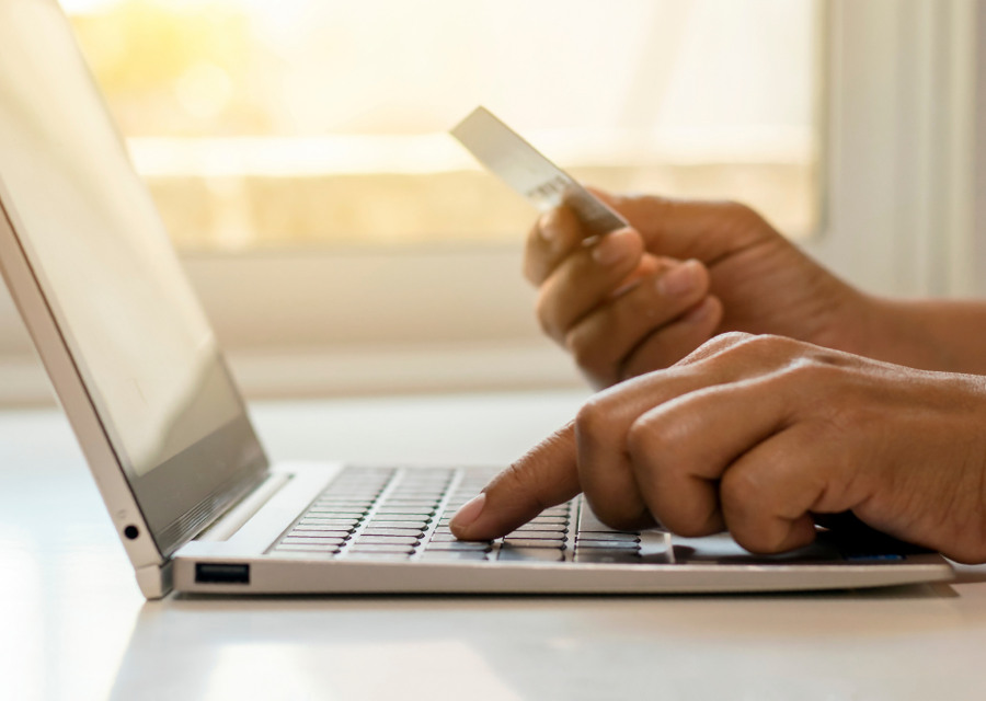 En person som håller i ett kreditkort och skriver på en bärbar dator.