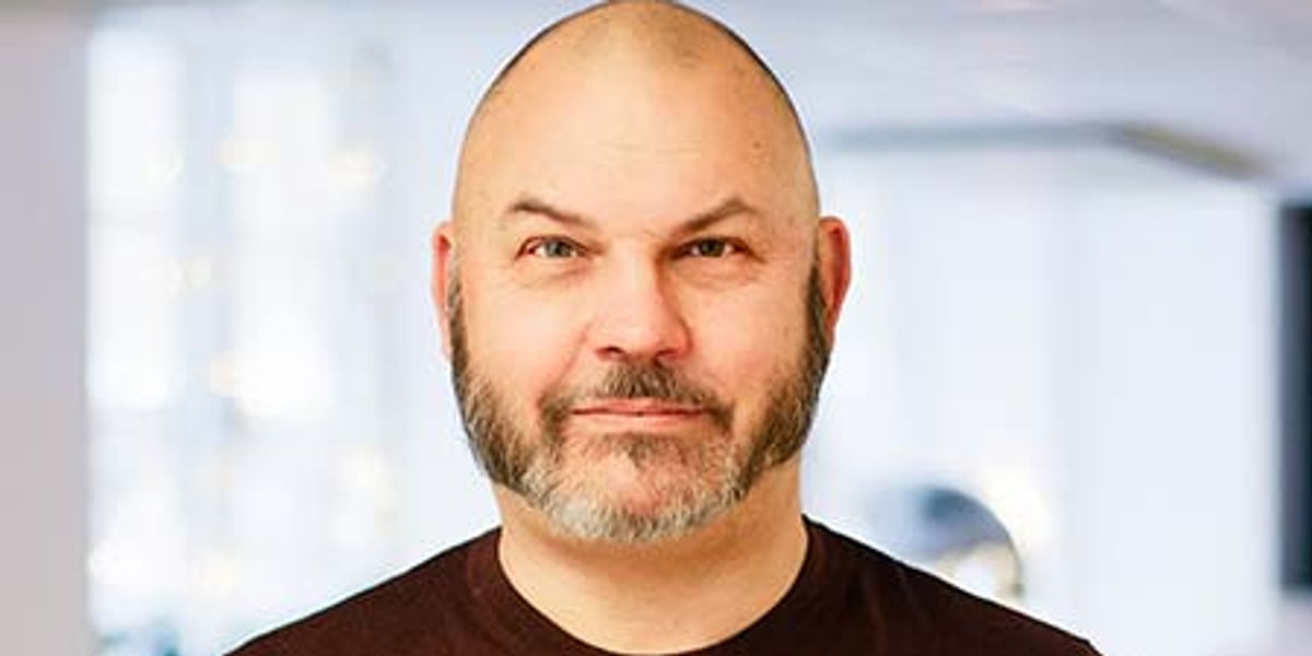 En man med skalligt huvud som bär en brun skjorta.