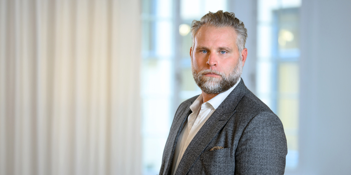 En man i kostym står framför ett fönster.