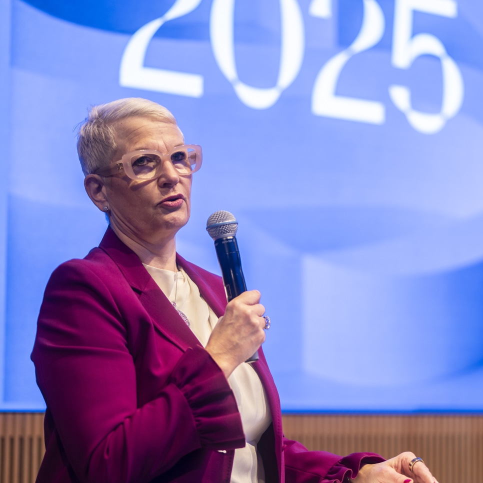 En kvinna talar i en mikrofon inför en folkmassa.