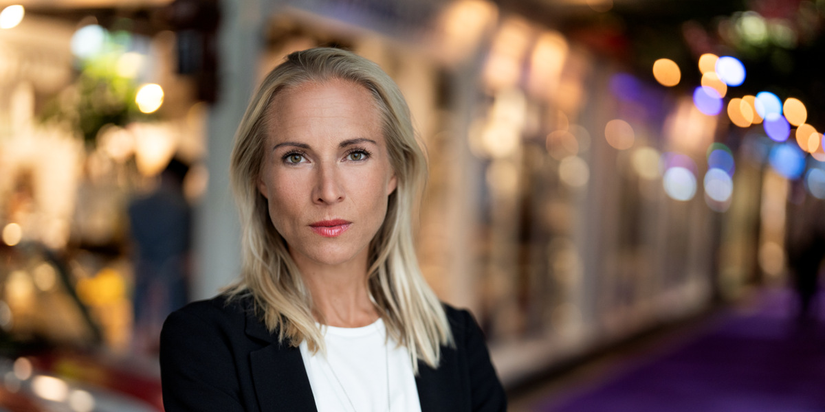 En kvinna med armarna i kors som står framför en bil.