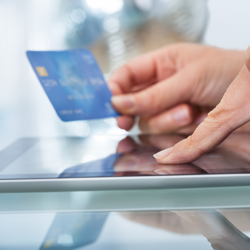 En person som håller i ett kreditkort medan han använder en surfplatta.