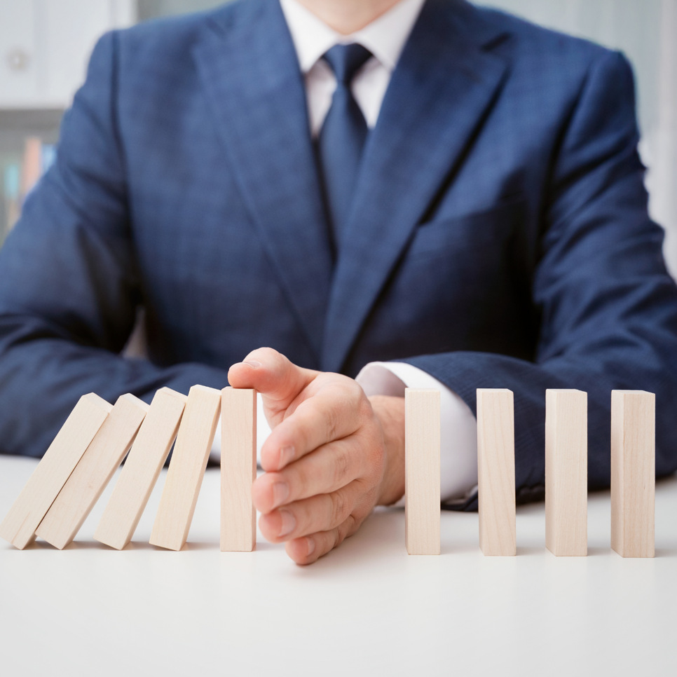 En kostymklädd man sitter vid ett bord med dominospel framför sig.