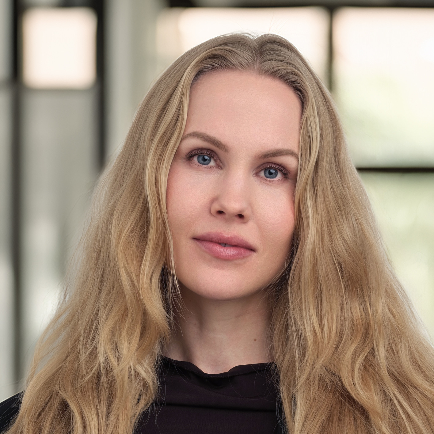 En kvinna med långt blont hår står framför ett fönster.