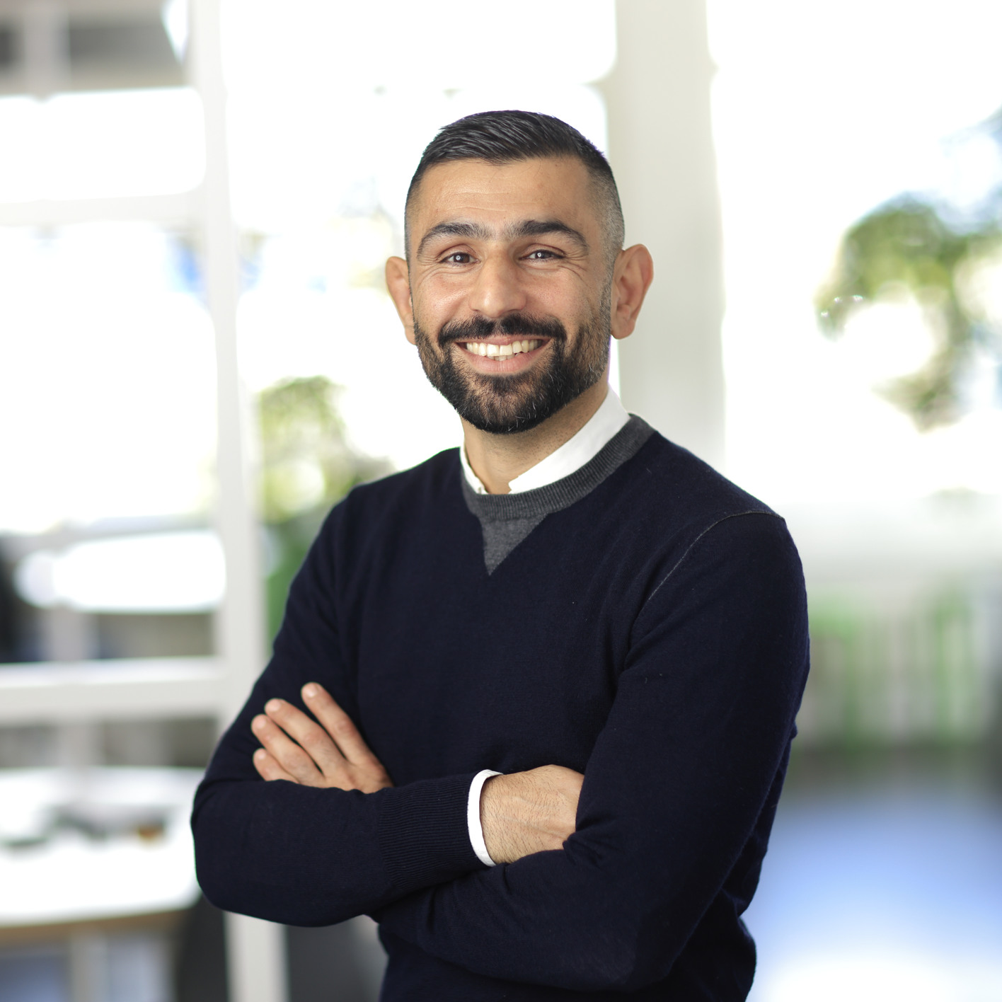 En man med armarna i kors står framför ett fönster.