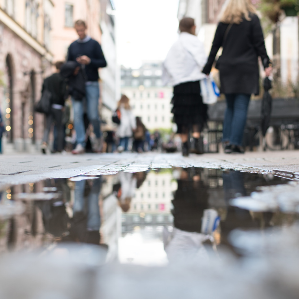 En grupp människor som går längs en gata bredvid en vattenpöl.