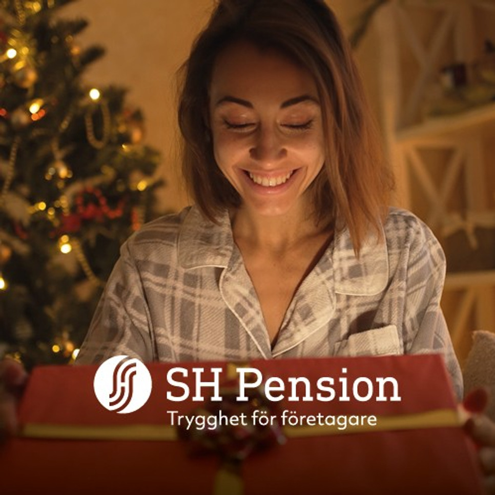 En kvinna öppnar en julklapp framför en julgran.