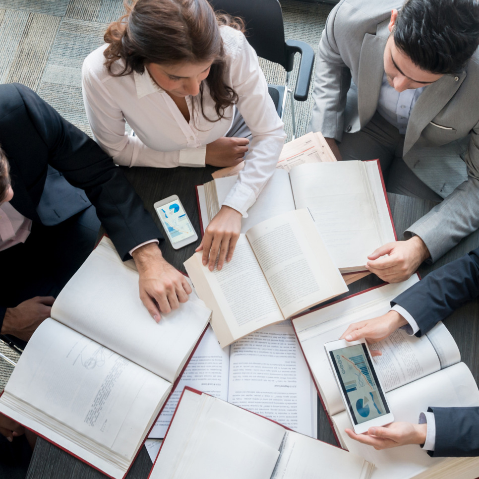 personer som sitter tillsammans runt ett bord fyllt med böcker och papper