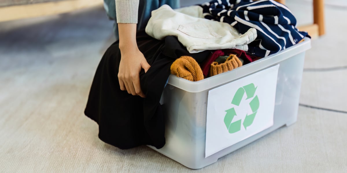 En kvinna sitter på golvet bredvid en låda fylld med kläder.