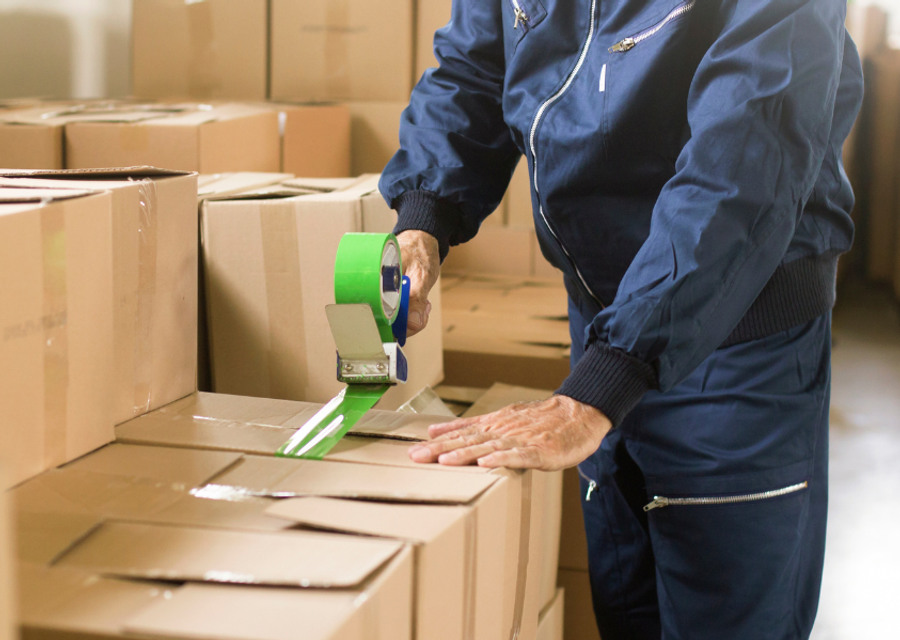 En man i en lagerlokal packar lådor med en grön tejp.