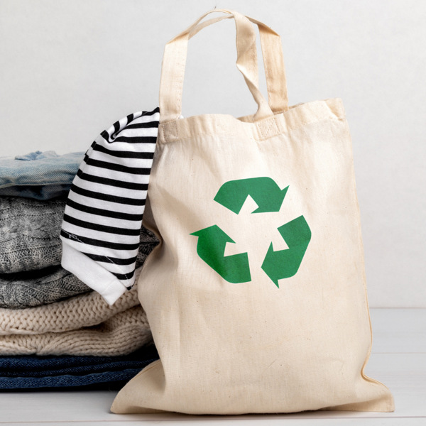 En påse med en återvinningssymbol på bredvid en hög med kläder.