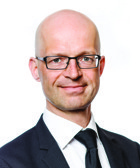 En man i kostym och slips som poserar för ett foto.