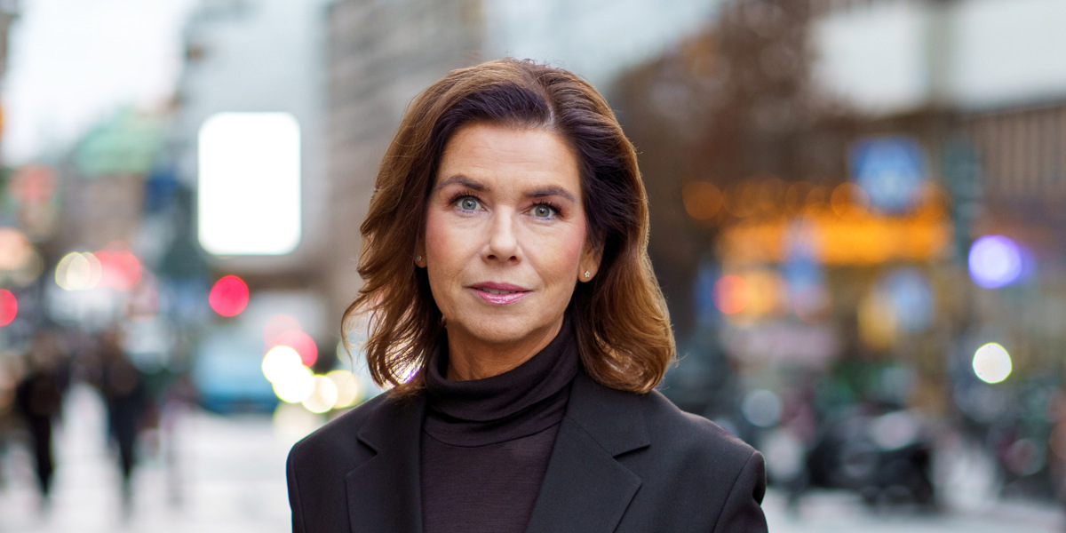 En kvinna i svart kostym står på en trottoar.