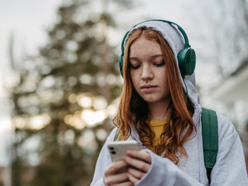 En flicka med hörlurar tittar på sin mobiltelefon.