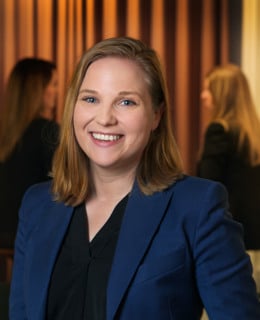 En kvinna i blå jacka står i ett rum.