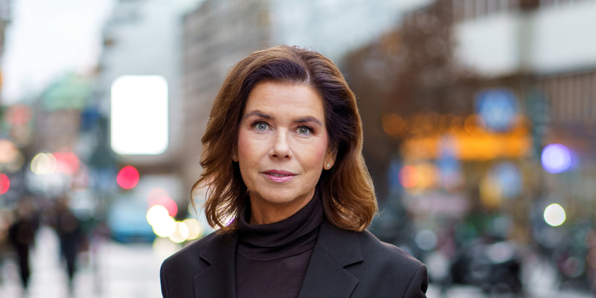En kvinna i svart kostym står på en trottoar.