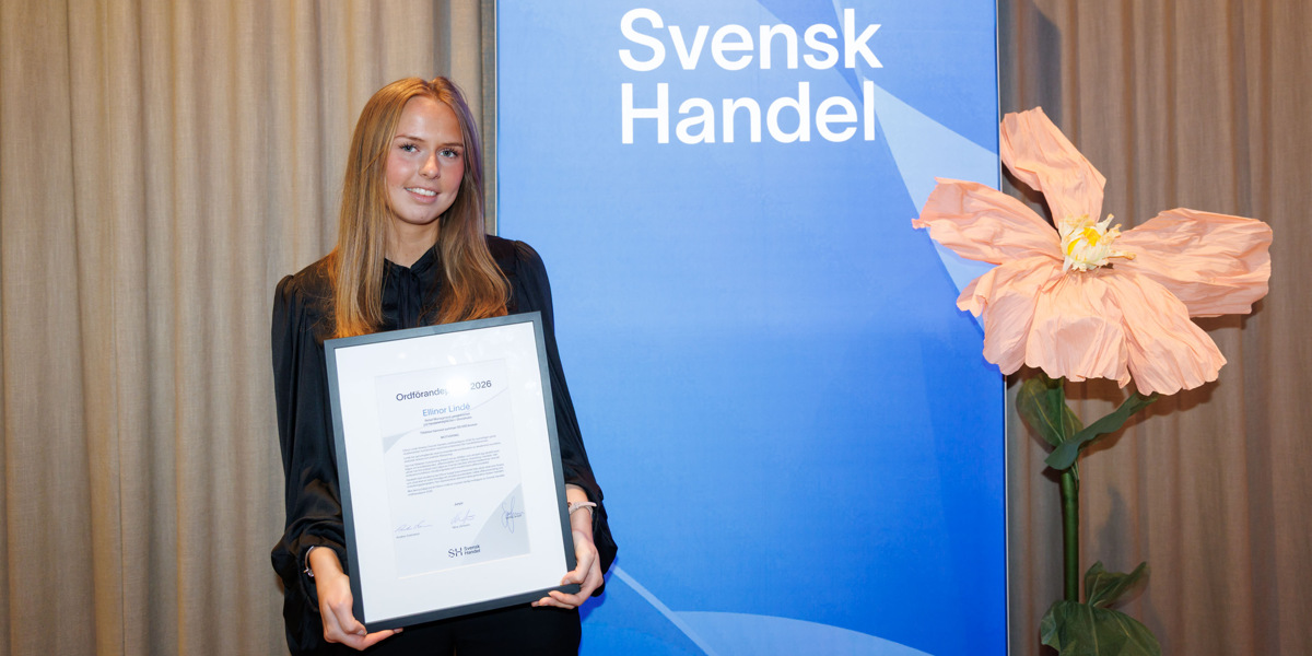En kvinna som h&aring;ller en plakett framf&ouml;r en skylt.