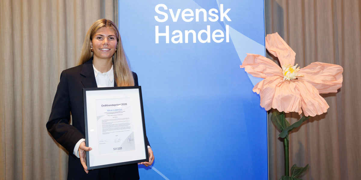 En kvinna som h&aring;ller en plakett framf&ouml;r en bl&aring; skylt.
