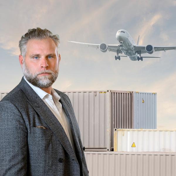 En man i kostym står framför ett flygplan.