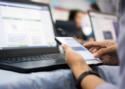 En person som sitter framför en bärbar dator och håller i en mobiltelefon.