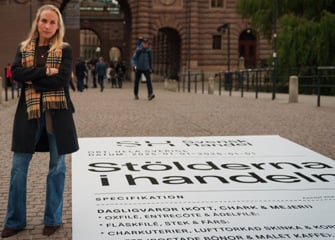 En kvinna står framför en skylt.