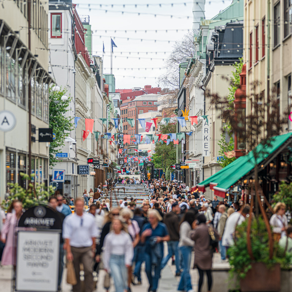 En folkmassa som går längs en gata bredvid höga byggnader.