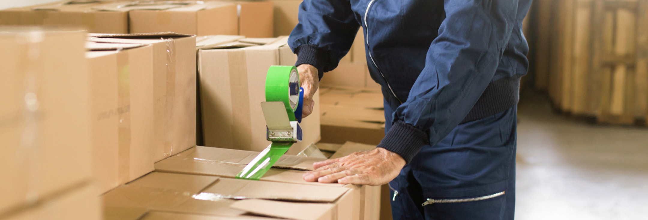 En man i en lagerlokal packar lådor med en grön tejp.