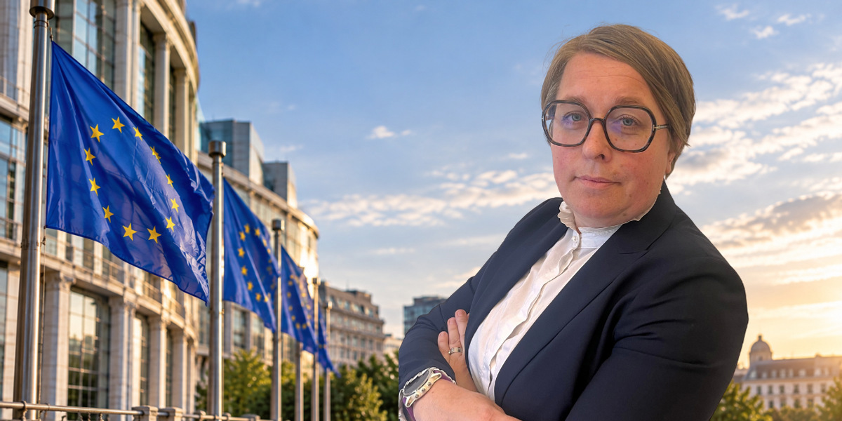 En kvinna i kostym och glasögon som står framför en europeisk flagga.