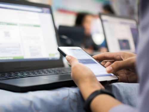 En person som sitter framför en bärbar dator och håller i en mobiltelefon.