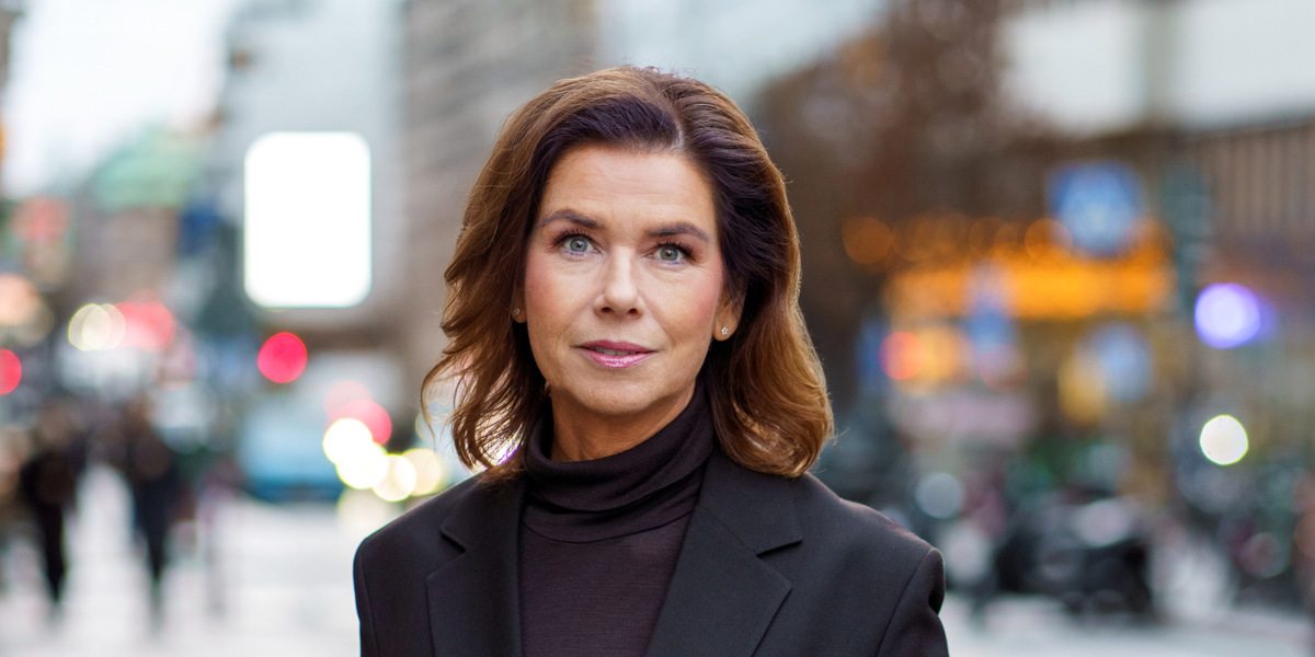 En kvinna i svart kostym står på en trottoar.