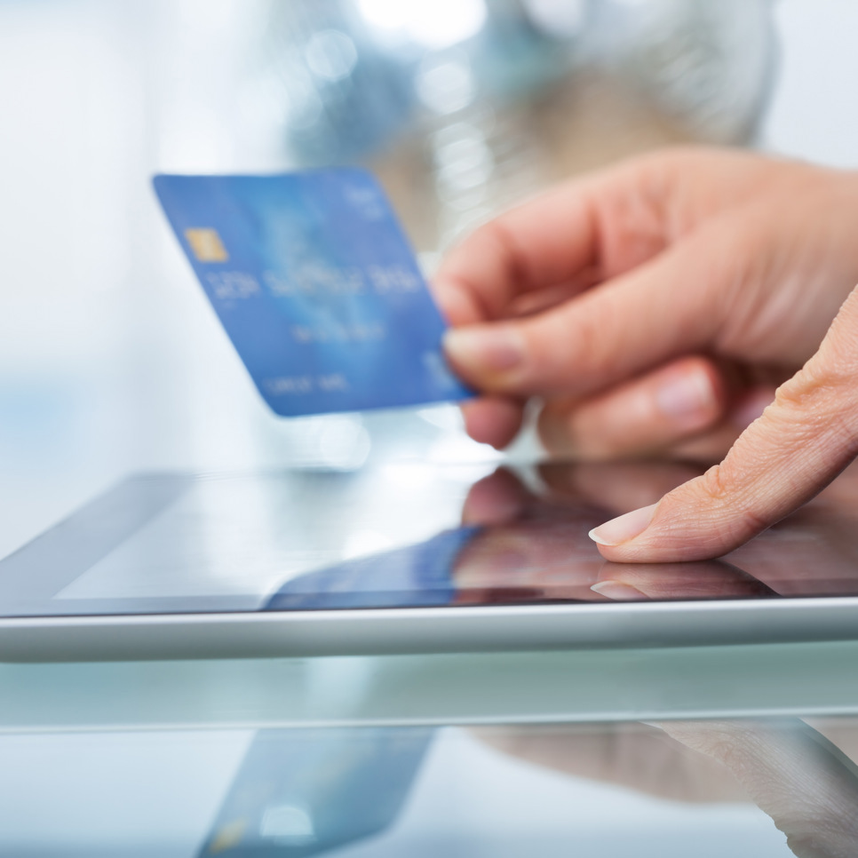 En person som håller i ett kreditkort medan han använder en surfplatta.
