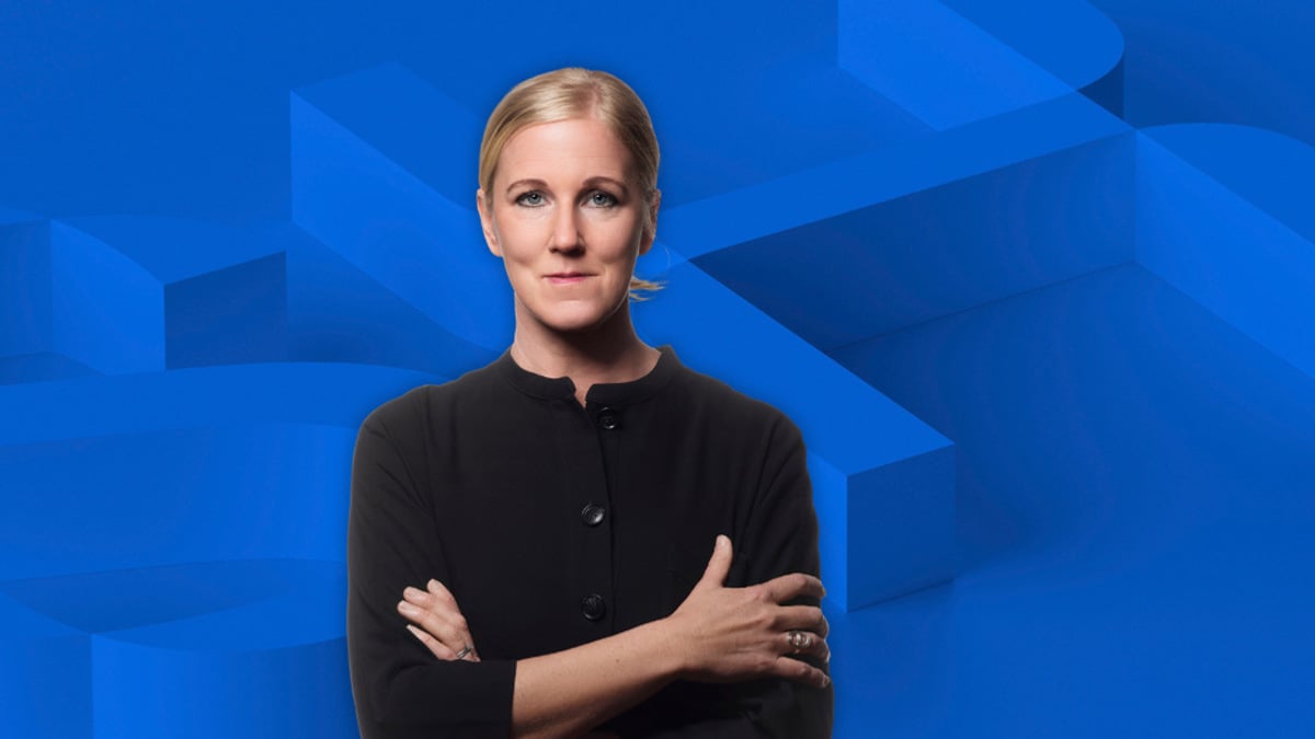 En kvinna står med armarna i kors framför en blå bakgrund.