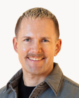 En man med mustasch ler för en bild.