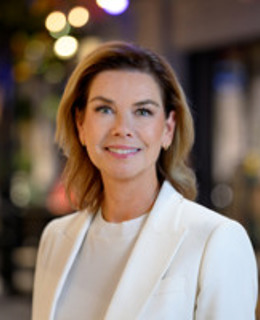 En kvinna i vit kostym står framför en byggnad.