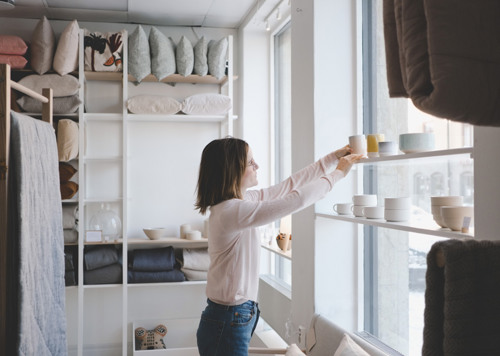 En kvinna står framför ett fönster och håller i en kopp.