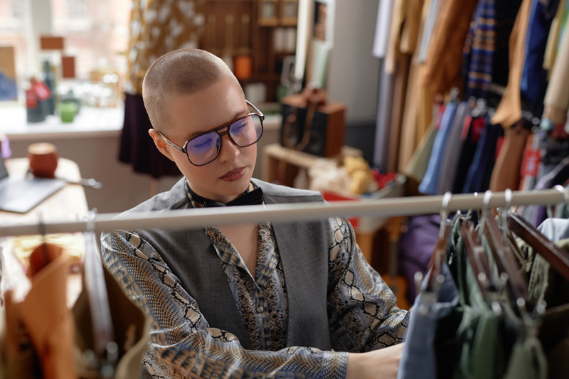 En man med glas&ouml;gon tittar p&aring; en skjorta p&aring; en hylla.