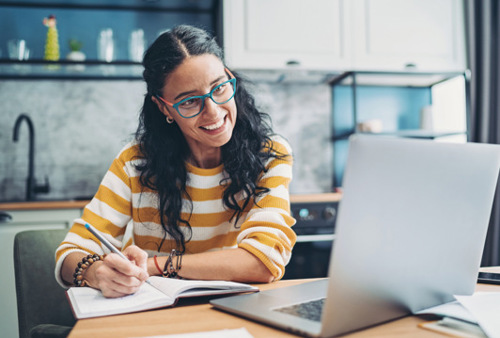 En kvinna sitter vid ett bord framför en bärbar dator.