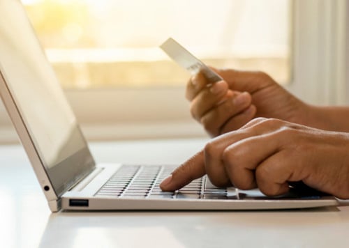 En person som håller i ett kreditkort och skriver på en bärbar dator.