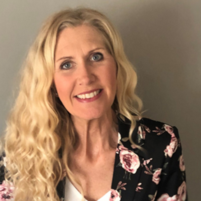 En kvinna med långt blont hår som bär en blommig jacka.