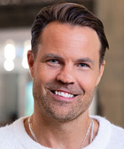 En man i en vit tröja som ler mot kameran.
