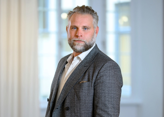 En man i kostym står framför ett fönster.