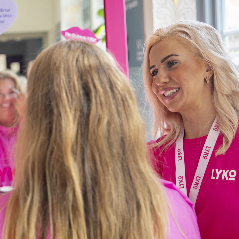 En kvinna i rosa skjorta står framför en spegel.