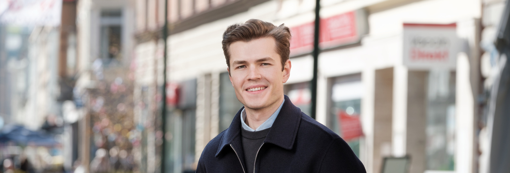 En man i svart jacka står på en trottoar.