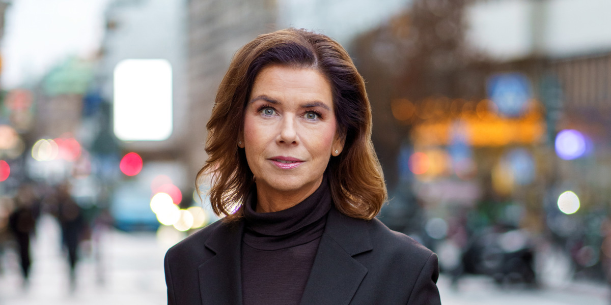 En kvinna i svart kostym står på en trottoar.