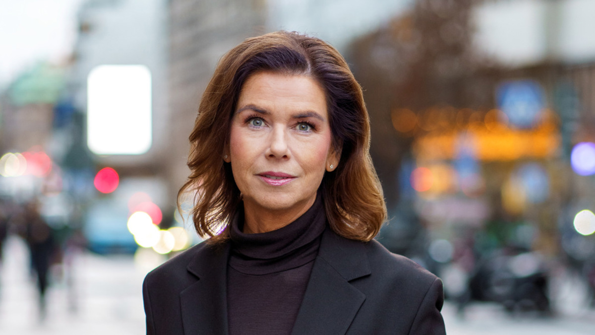 En kvinna i svart kostym står på en trottoar.