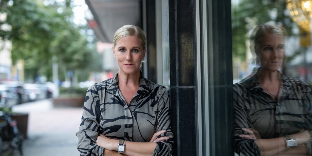 En kvinna som st&aring;r framf&ouml;r ett f&ouml;nster med armarna i kors.